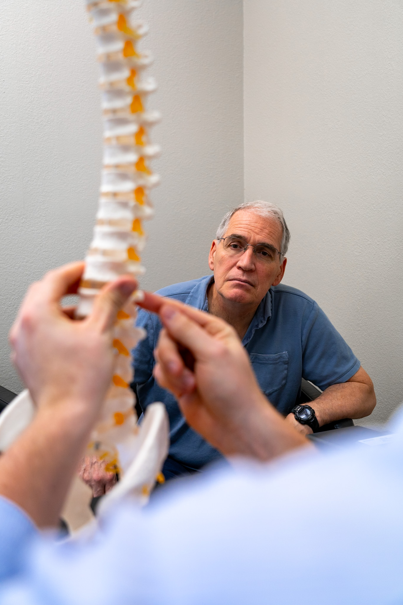Older man listening to chiropractor explain spinal model during consultation at Vita Nova Chiropractic in Plano, TX