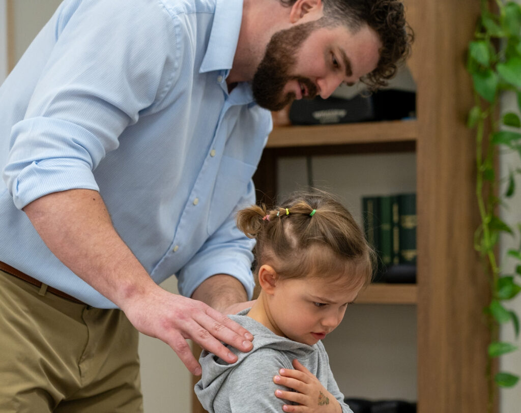 Pediatric chiropractor gently assessing a young child’s spine to address torticollis and improve neck mobility