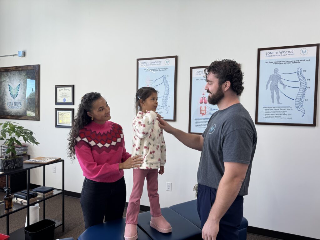 A chiropractor interacts gently with a young child and her mother during a consultation in Plano, TX, highlighting a caring approach for children with autism.