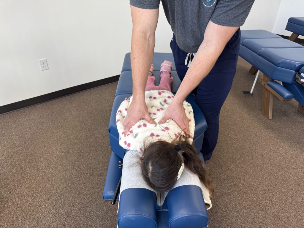 Chiropractor performing a gentle spinal adjustment on a young child in a clinic setting to support bed wetting issues in Plano.