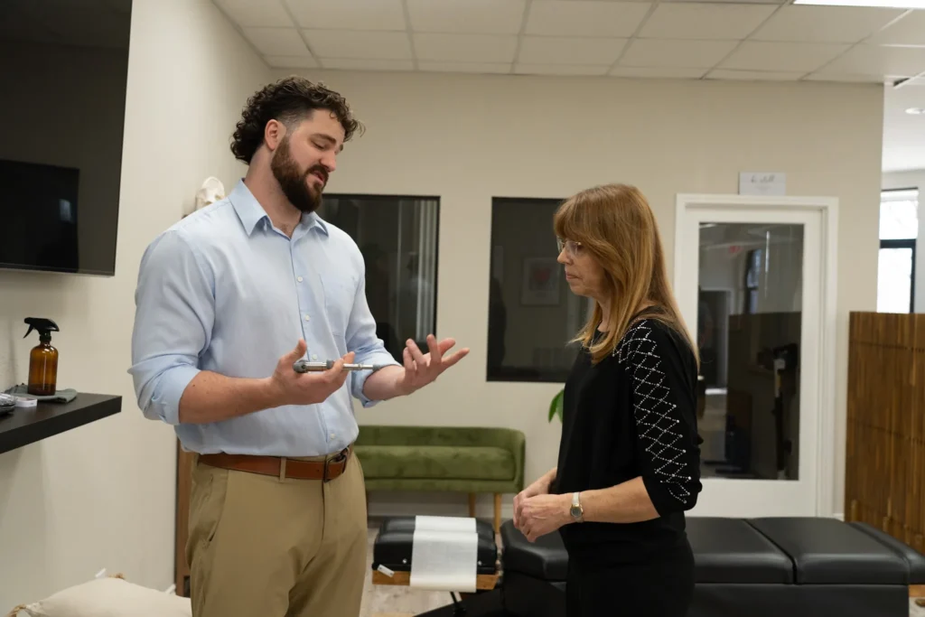 Dr. Korrin Taylor holds an adjusting instrument while speaking with a patient in a treatment room.