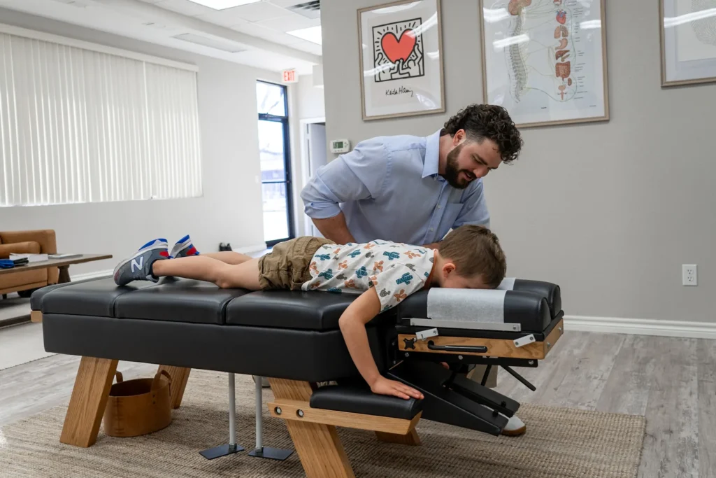 Dr. Korrin Taylor smiles while examining a young boy lying on a chiropractic adjustment table.