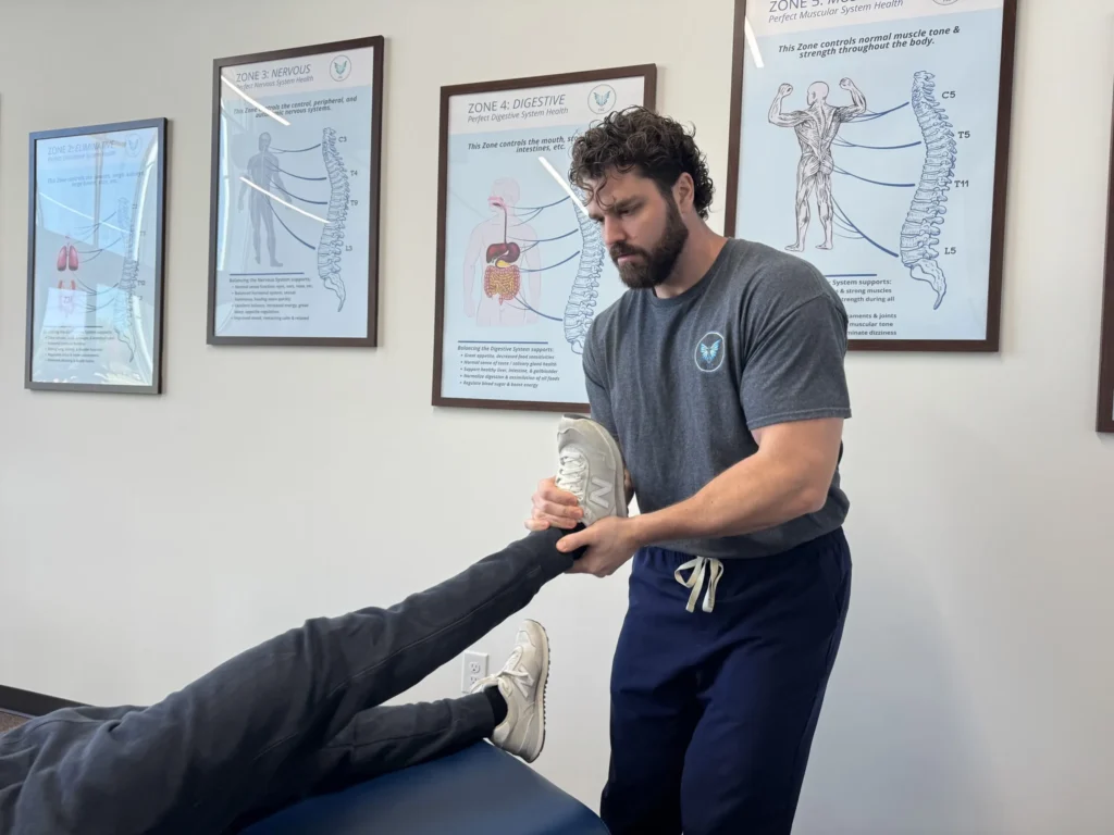 Dr. Korrin Taylor lifts and assesses a patient's leg on an adjustment table in an exam room.