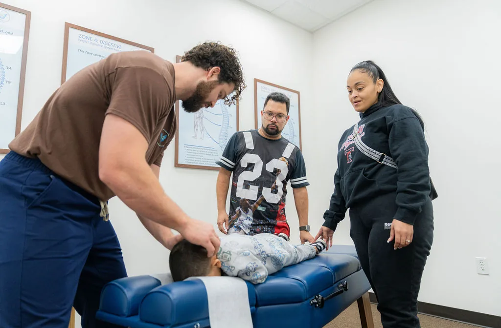 Dr. Korrin Taylor gently adjusts a child's neck on a treatment table while the child's parents observe.