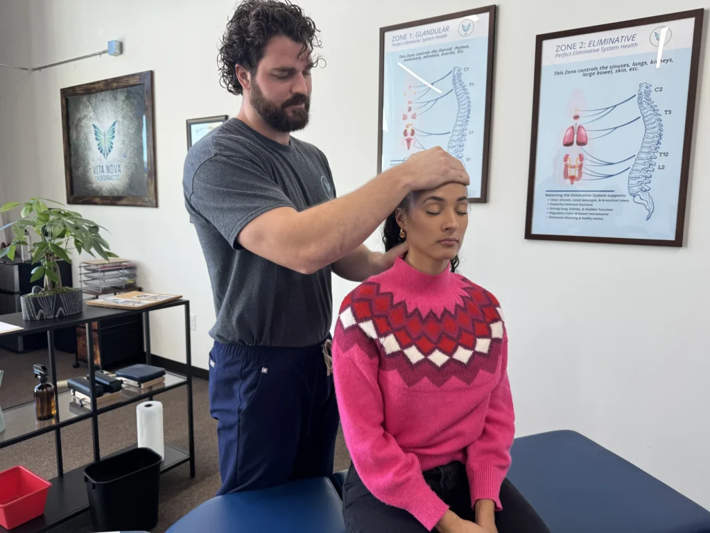 Dr. Korrin Taylor places his hands on a seated patient's forehead and neck during an examination.