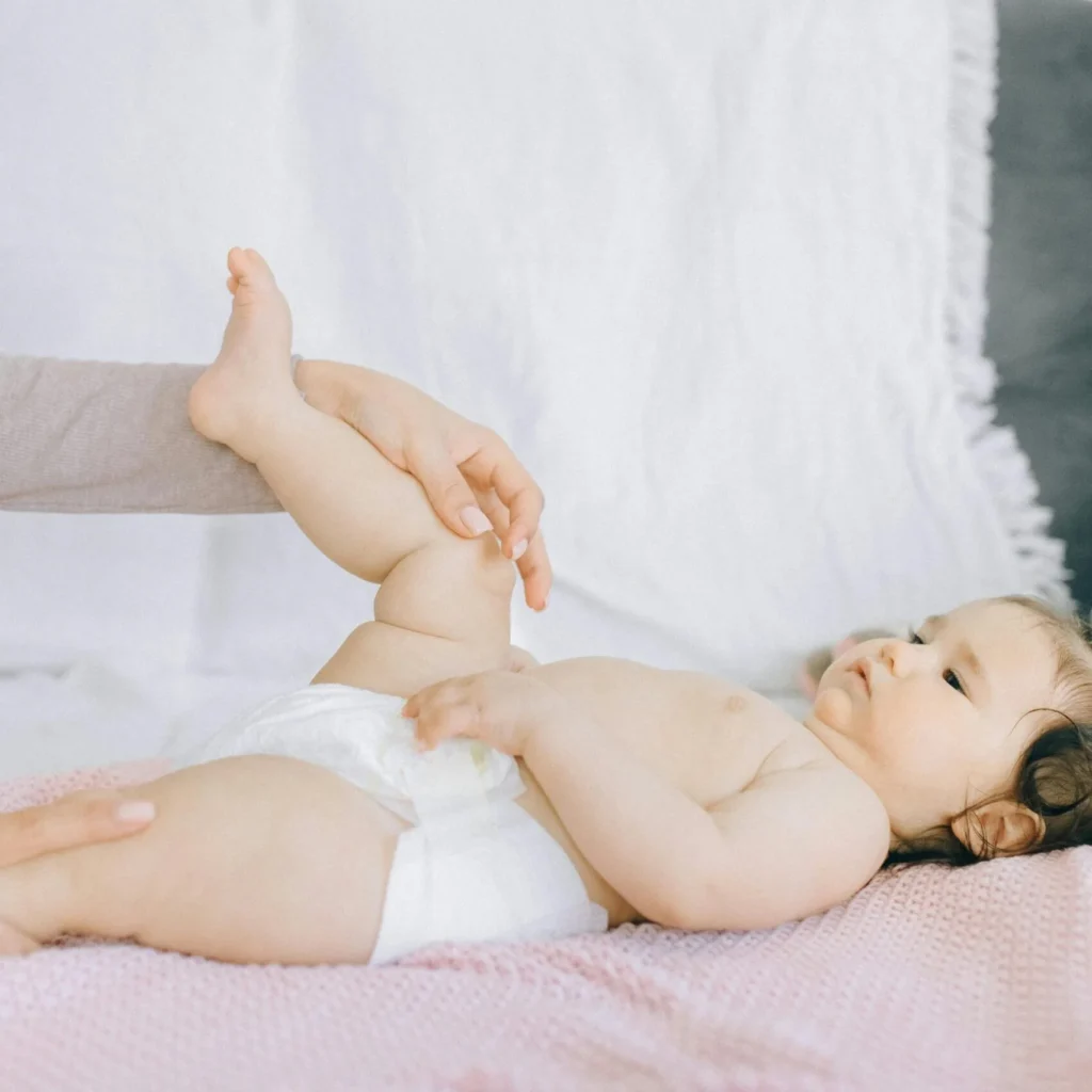 An infant lying on a pink blanket while an adult gently supports and lifts the baby's leg.