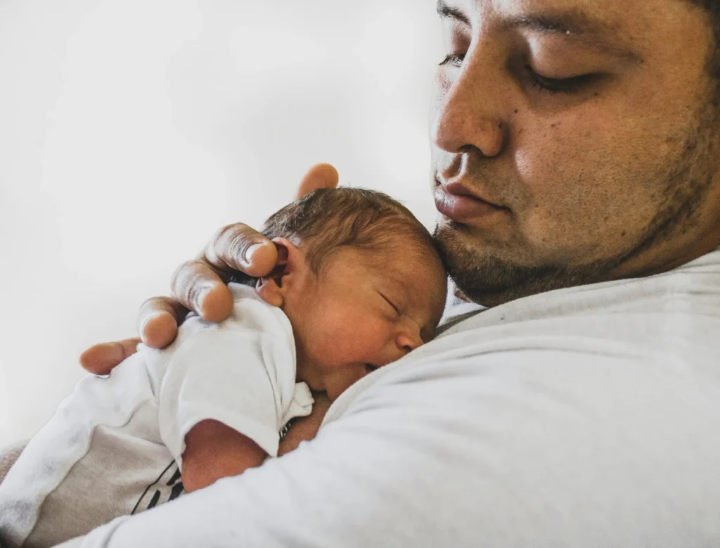 Close-up of a man gently holding a sleeping newborn baby against his chest.