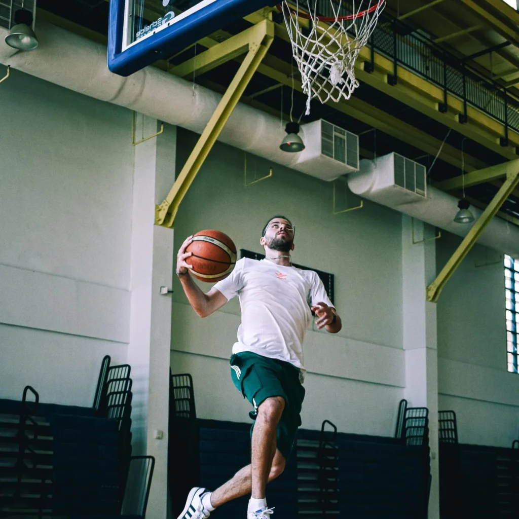 Young man leaping toward an indoor basketball hoop holding a basketball.