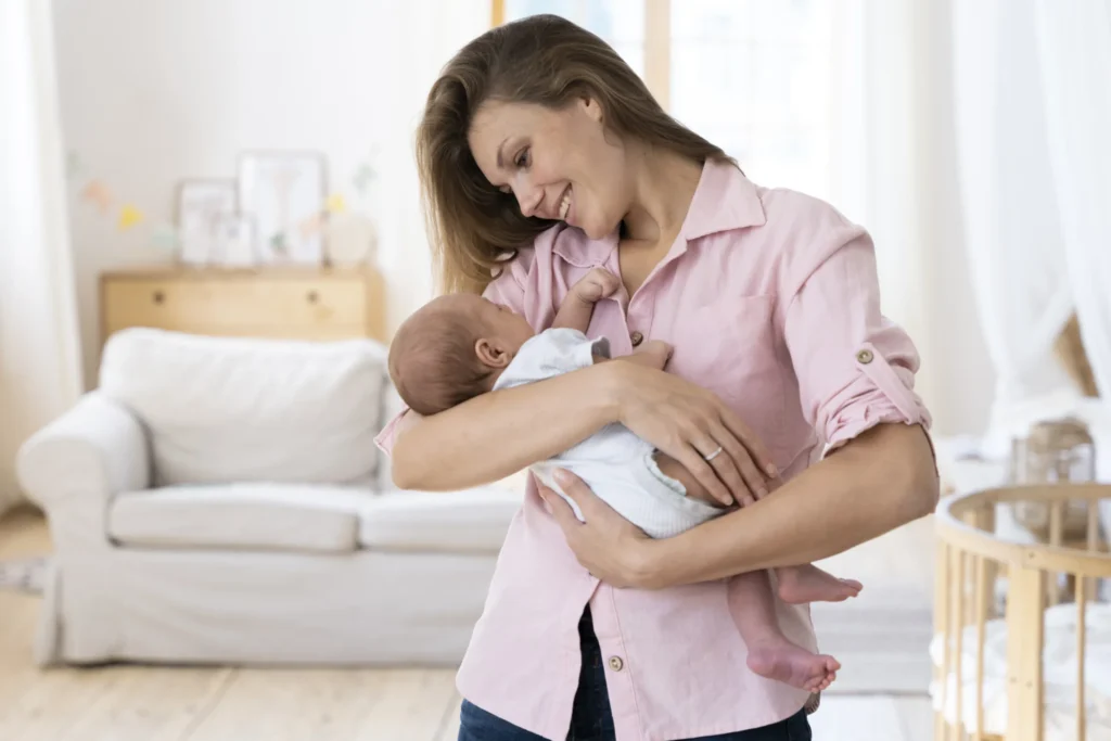 Smiling mother gently cradling her newborn baby in a bright living room.
