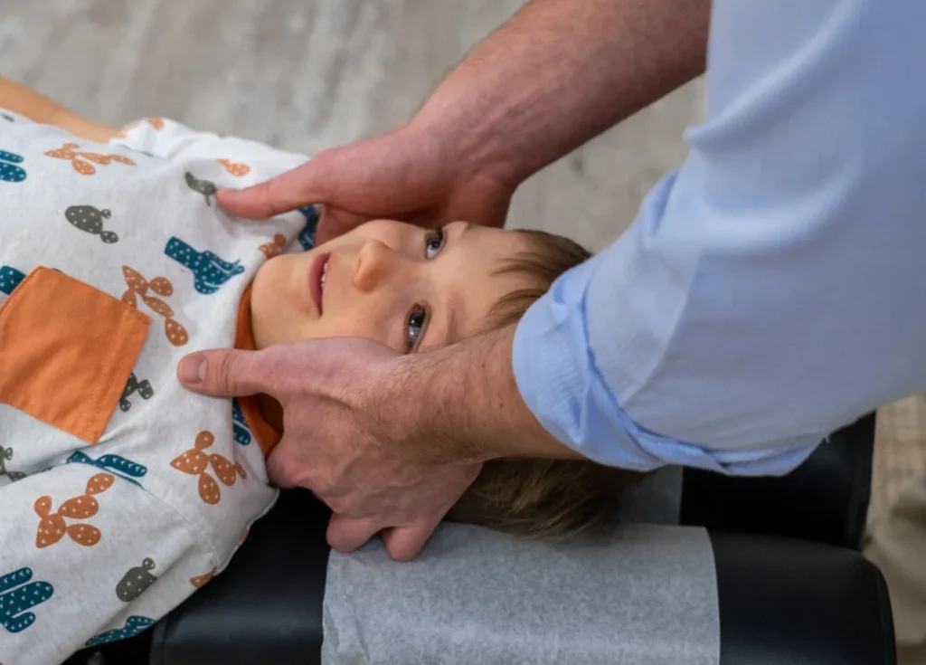 Chiropractor gently holding the neck and head of a young child lying on an adjusting table.